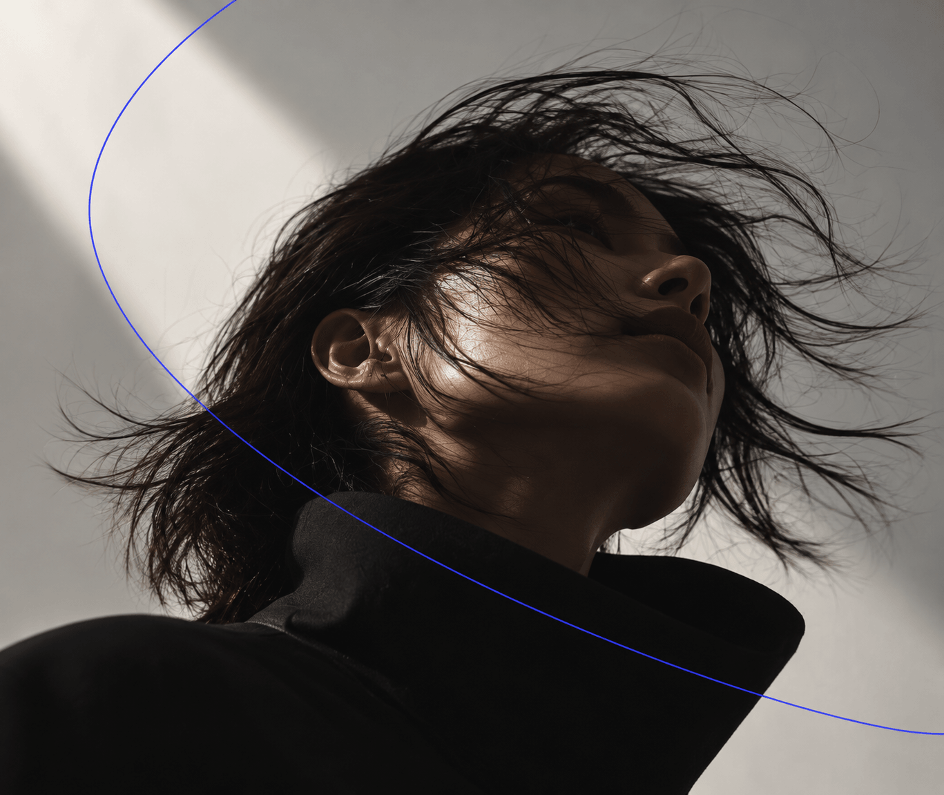 Portrait looking up, hair caught mid-motion, crossed by a thin blue line